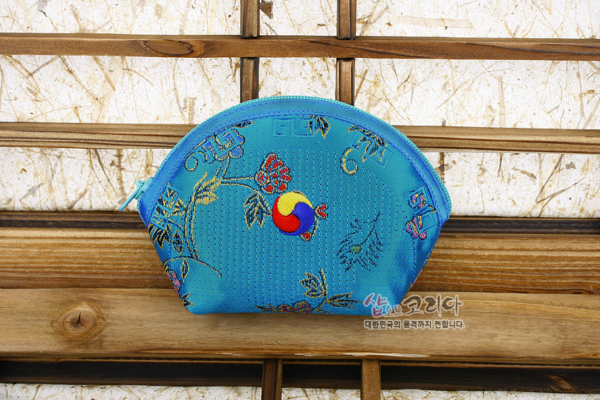 [텍스트: 샵오브코리아 대한민국의 품격까지 전합니다.] 청색 비단 누비 원단에 태극 문양과 꽃·덩굴 자수가 놓인 반원형 지퍼 동전지갑 모습