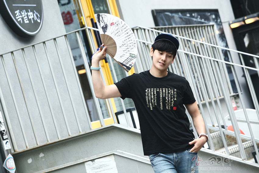 [텍스트: 족발센터] 검은색 면 티셔츠 위에 금색 훈민정음 서체를 세로 배열한 입체 발포 문양과 한글 필체가 적힌 전통 부채를 든 모습 표현