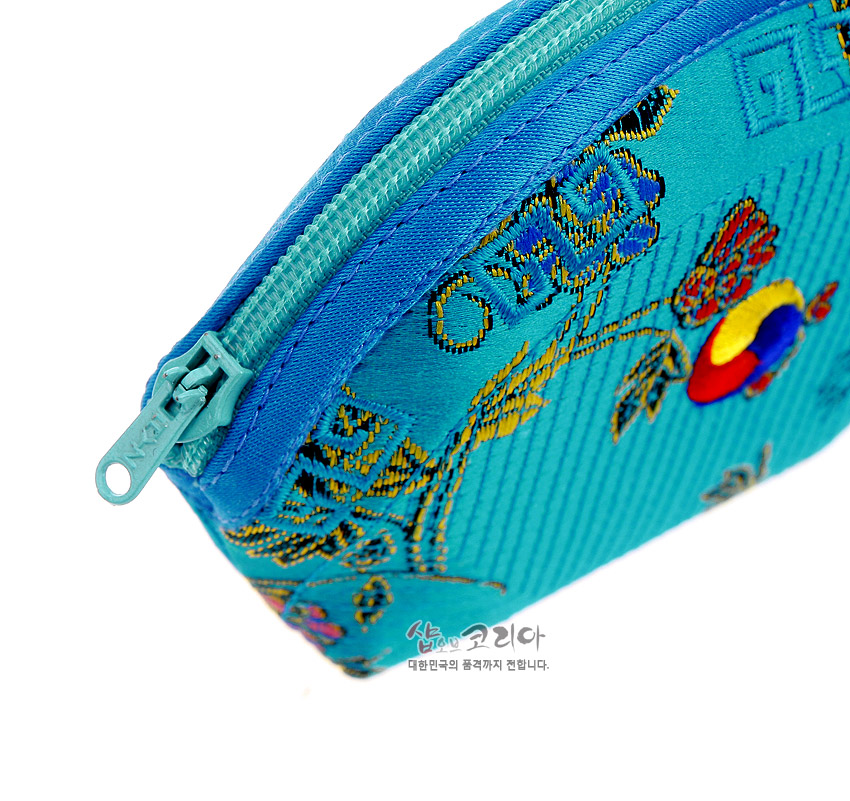 [텍스트: 샵오브코리아 대한민국의 품격까지 전합니다.] 청색 비단 누비 원단 위에 태극문양과 꽃·덩굴 자수를 놓고 청록색 지퍼를 더한 반원형 동전지갑 클로즈업 이미지