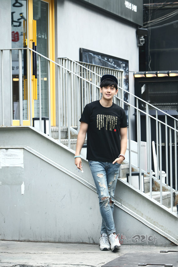 [텍스트: 훈민정음 해례본 한글 구절과 붉은색 낙관 인장] 검은색 면 티셔츠 위에 금색 입체발포 기법으로 훈민정음 서체를 세로로 배치한 현대적인 스트리트 스타일 연출 모습