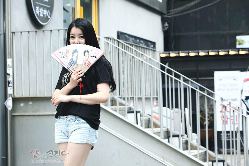 [텍스트: 샵오브코리아] 검은색 반소매 티셔츠 위에 금색 훈민정음 입체 발포 문양을 넣어 입체감을 살린 캐주얼 코디 연출 모습