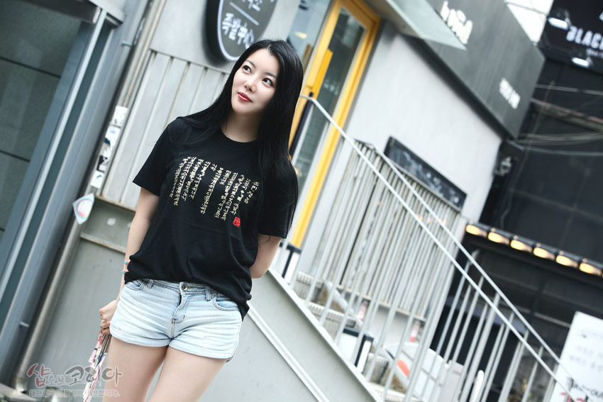 [텍스트: 샵오브코리아] 흑색 면 티셔츠 위 금색 훈민정음 서체를 입체 발포 기법으로 표현한 사각형 전통 문자 문양 디자인