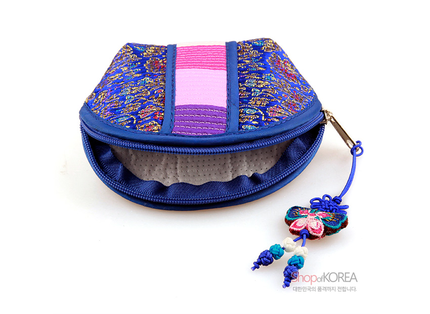 [텍스트: shopofKOREA 대한민국의 품격까지 전합니다.] 감색 비단 바탕에 금색 전통 문양과 분홍·보라색 색동 누비 장식, 나비 모양 매듭 장식이 달린 반달 형태 동전지갑 모습