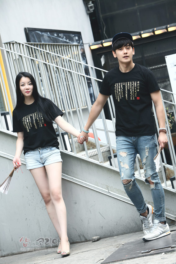 [텍스트: 훈민정음] 검은색 면 티셔츠 위에 금색 입체 발포 기법으로 새긴 세로형 훈민정음 서체와 붉은 낙관 문양이 배치된 캐주얼 코디 연출 이미지