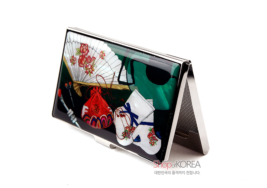 [텍스트: ShopofKOREA 대한민국의 품격까지 전합니다.] 흑색 옻칠 바탕에 자개 느낌의 초록색 배경, 꽃무늬 부채와 버선, 복주머니를 다채로운 색감으로 채색한 금속 명함케이스 디자인