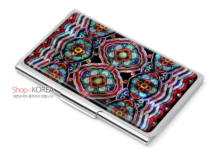 [텍스트: ShopofKOREA 대한민국의 품격까지 전합니다.] 금속 재질 위 자개 상감 기법으로 표현된 기와 단청 꽃무늬와 다채로운 적·청·록색 곡선 문양의 명함집 이미지 설명
