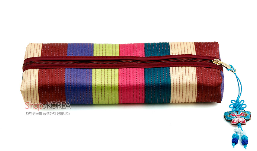 [텍스트: Shop of KOREA 대한민국의 품격까지 전합니다.] 색동 누비 기법의 다색 원단을 가로줄로 배치한 직사각형 필통과 붉은 지퍼, 청색 나비 매듭 장식 디테일 모습