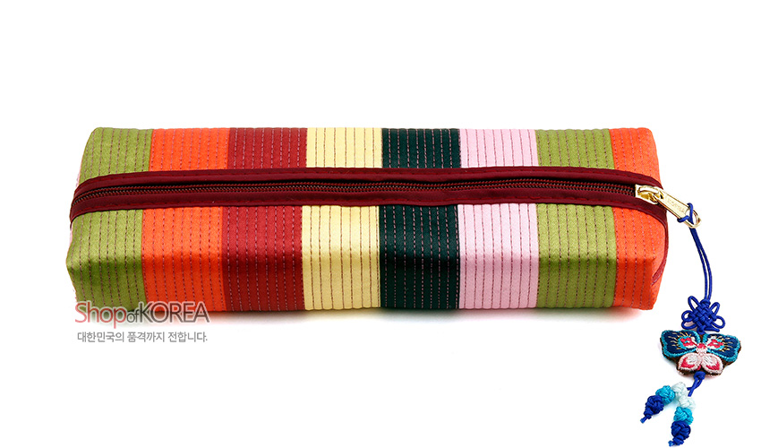 [텍스트: Shop of KOREA / 대한민국의 품격까지 전합니다.] 알록달록 색동 누비 원단으로 구성된 직사각형 필통, 와인색 지퍼와 금속 장식, 파랑 매듭과 나비 자수 장식 포인트 디자인