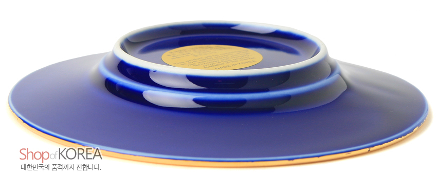 [텍스트: Shop of KOREA 대한민국의 품격까지 전합니다.] 짙은 청색 유약 처리된 금속 장식 접시의 바닥면과 중앙 금색 원형 라벨 디테일 표현
