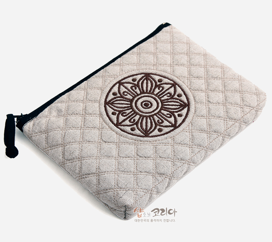 [텍스트: 샵오브코리아 대한민국의 품격까지 전합니다] 베이지색 누빔 천 소재에 갈색 고구려 수막새 연꽃 문양 자수를 더한 사각형 지퍼 파우치 디자인