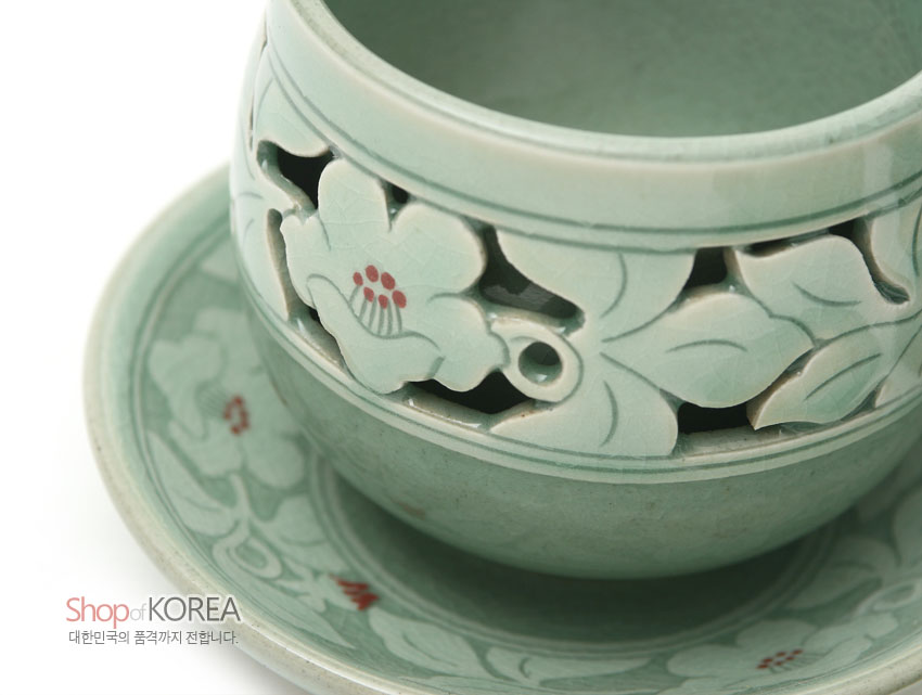 [텍스트: Shop of KOREA 대한민국의 품격까지 전합니다.] 연한 비취색 청자 위 투각 기법으로 표현된 무궁화와 잎사귀 문양, 붉은 포인트가 더해진 찻잔과 받침 구성