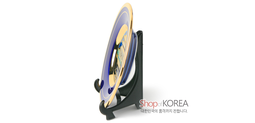 [텍스트: Shop of KOREA / 대한민국의 품격까지 전합니다.] 청색 바탕 위 금장 메탈릭 광택의 원형 접시와 검정색 플라스틱 받침대 측면 전시 장식 모습