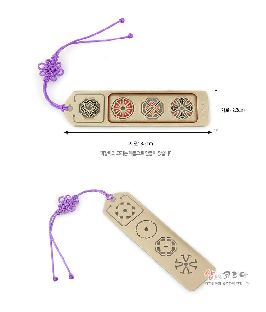 [텍스트: 세로: 8.5cm, 가로: 2.3cm, 책갈피의 고리는 매듭으로 만들어 졌습니다.] 금장 금속 재질 위에 붉은색·검은색 창살기와 전통 문양 상감, 보라색 매듭끈 장식 책갈피 모습