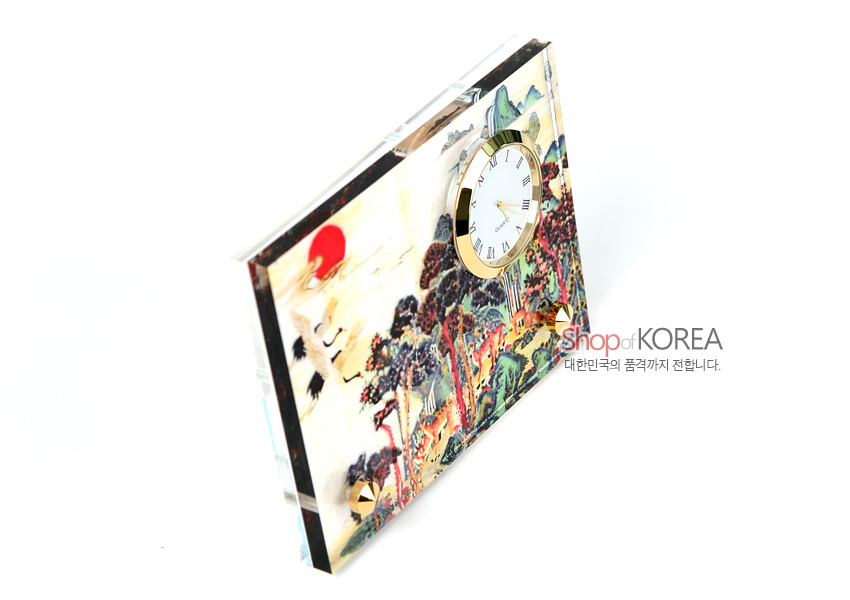 [텍스트: Shop of KOREA 대한민국의 품격까지 전합니다.] 자개 느낌 광택 판 위 민화풍 십장생 산수와 해, 소나무를 채색하고 금색 메탈 테두리 원형 시계를 배치한 탁상용 시계 이미지