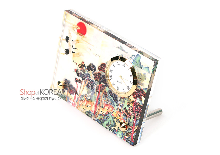 [텍스트: Shop of KOREA / 대한민국의 품격까지 전합니다.] 자개 느낌 광택 판 위에 십장생 민화풍 산수와 학, 붉은 해를 채색하고 금색 금속 테두리 원형 시계를 더한 탁상용 시계 이미지