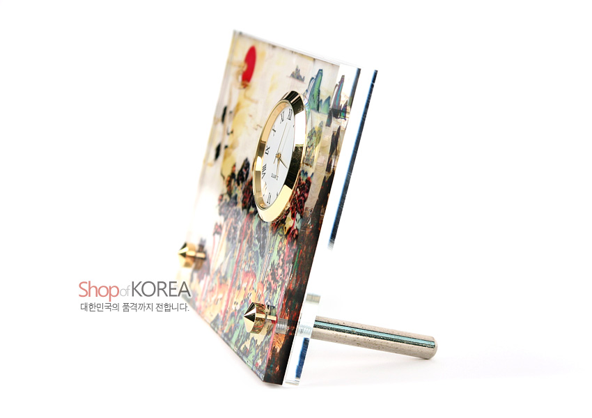 [텍스트: Shop of KOREA 대한민국의 품격까지 전합니다.] 투명 아크릴 판 위에 칠보풍 십장생 산수 문양과 금색 금속 테두리 원형 시계가 결합된 탁상용 시계 이미지