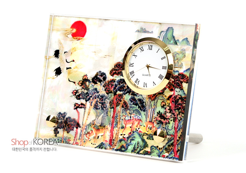 [텍스트: Shop of KOREA / 대한민국의 품격까지 전합니다. / QUARTZ] 자개 바탕에 옻칠된 십장생 민화 산수·학·사슴 문양과 금색 금속 테두리 원형 시계가 조화를 이룬 탁상용 시계 이미지 설명