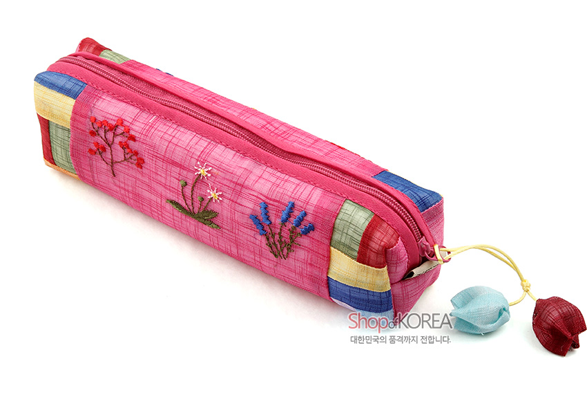 [텍스트: Shop of KOREA 대한민국의 품격까지 전합니다.] 분홍 모시 천에 꽃자수와 오방색 조각천 배색, 조개 모양 매듭 장식 지퍼 손잡이가 돋보이는 직사각형 필통 디자인