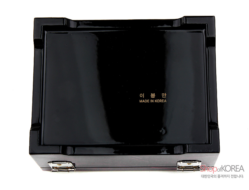 [텍스트: 이 봉 만 / MADE IN KOREA] 광택 있는 흑색 옻칠 표면과 금색 각인, 일자형 금속 경첩으로 마감된 직사각 보석함 바닥면 모습