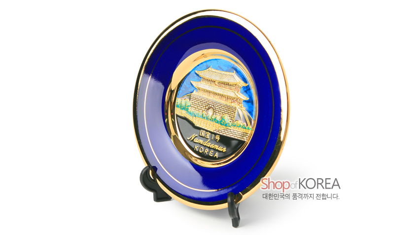 [텍스트: Namdaemun KOREA] 진한 청색 바탕과 금색 테두리에 24K 도금 입체 남대문 전경을 양각으로 표현한 금속 장식 접시 형태