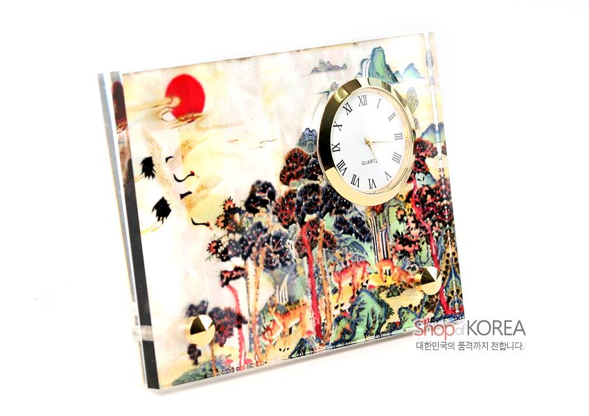 [텍스트: Shop of KOREA 대한민국의 품격까지 전합니다.] 자개 바탕 위 옻칠 처리된 십장생 민화 산수·학·사슴·해 문양과 금빛 금속 테두리 원형 시계가 조화를 이룬 탁상용 시계 이미지 설명