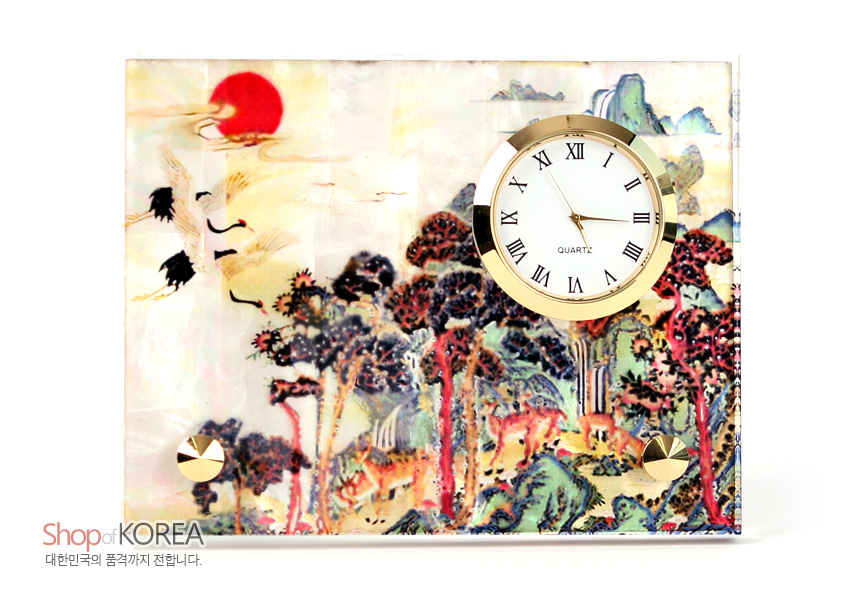 [텍스트: Shop of KOREA / QUARTZ] 자개 바탕 옻칠 위에 붉은 해와 학, 소나무와 사슴이 그려진 십장생 민화 문양과 금색 금속 테두리 원형 시계가 조화를 이룬 탁상용 시계 이미지설명