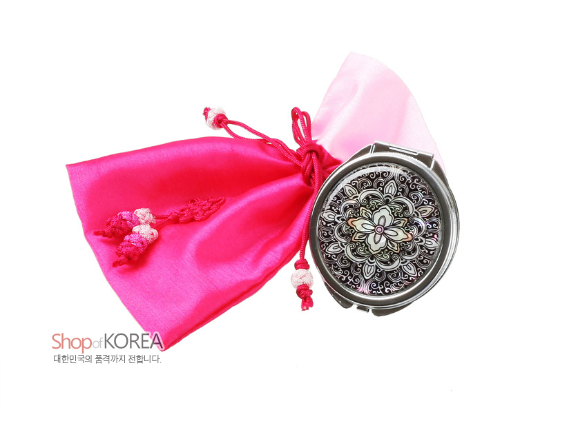 [텍스트: Shop of KOREA 대한민국의 품격까지 전합니다.] 자개로 연꽃문을 섬세하게 상감한 금속 손거울과 분홍색 비단 복주머니, 매듭 장식 조화 이미지