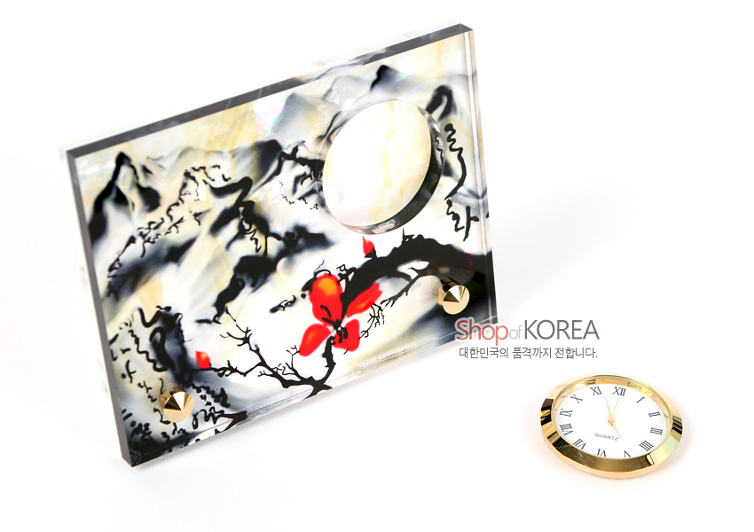 [텍스트: Shop of KOREA, 대한민국의 품격까지 전합니다.] 자개 바탕 위 수묵 산수도와 붉은 매화 문양이 채색된 직사각형 시계 받침과 금속 테두리 분리형 원형 시계 구성