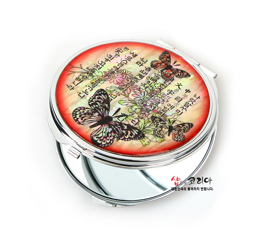 [텍스트: 샵오브코리아 대한민국의 품격까지 전합니다.] 붉은 그러데이션 배경 위 자개 상감 나비·꽃 문양과 훈민정음 글귀가 장식된 금속 양면 손거울 디자인