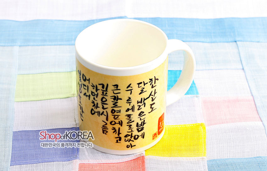 [텍스트: Shop of KOREA / 대한민국의 품격까지 전합니다] 아이보리 도자 머그컵에 옅은 노란 바탕과 검은 한글 서예 문양, 붉은 낙관이 둘러진 디자인