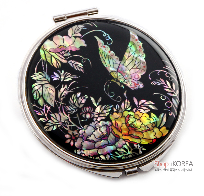 [텍스트: Shop of KOREA 대한민국의 품격까지 전합니다.] 검은 옻칠 바탕 위에 오색 자개 상감으로 표현된 큼직한 나비와 모란, 꽃과 잎이 섬세하게 어우러진 원형 금속 손거울 디자인