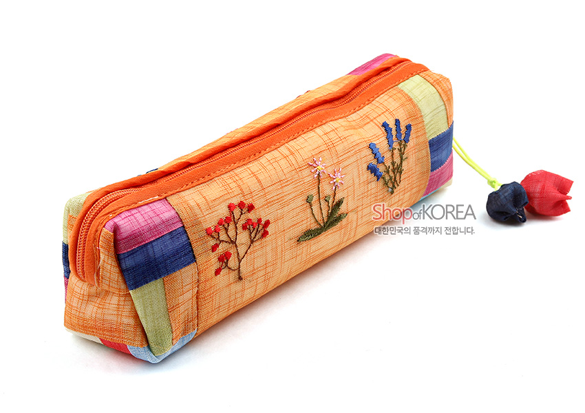 [텍스트: Shop of KOREA 대한민국의 품격까지 전합니다.] 황색 모시 원단 위에 붉은색·분홍색·파란색 꽃자수와 색동 조각천 배색, 조개 모양 매듭 장식이 어우러진 누비 필통 디자인