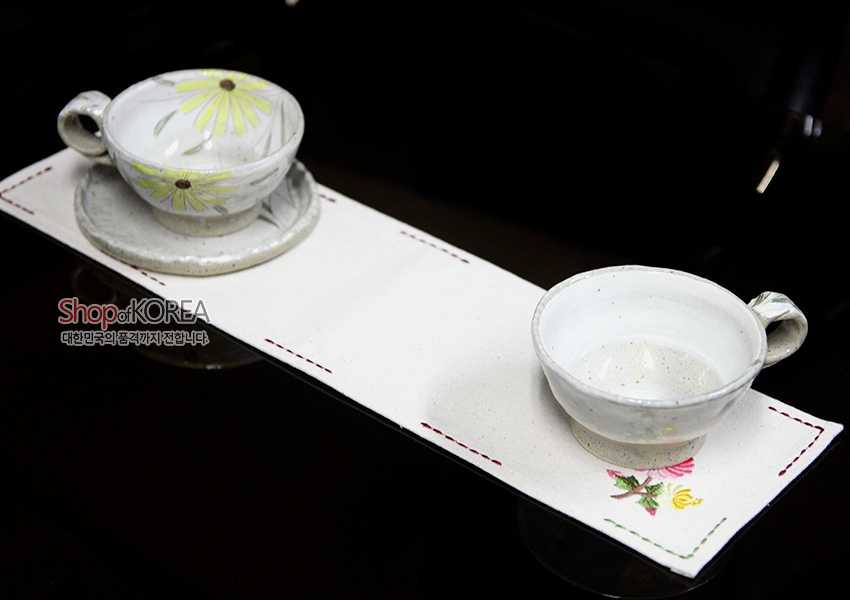 [텍스트: Shop of KOREA 대한민국의 품격을 전합니다] 광목 재질 긴 직사각형 런너형 식탁보, 가장자리 색실 스티치와 끝부분 분홍·노랑 국화 자수 문양 장식 이미지