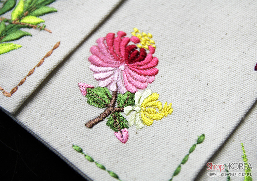[텍스트: Shop of KOREA 대한민국의 공예까지 전합니다.] 광목 바탕에 분홍·노랑 국화와 잎사귀를 실선 자수 기법으로 놓은 전통 문양 식탁보 디테일 컷