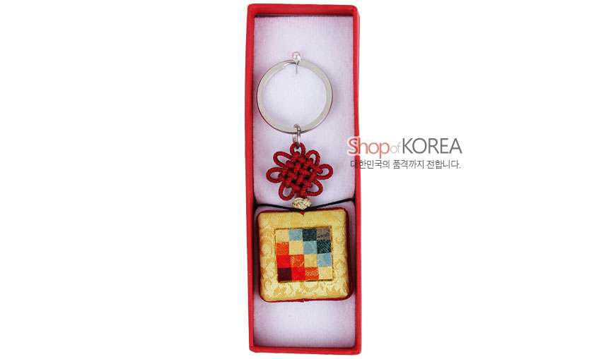 [텍스트: Shop of KOREA 대한민국의 품격까지 전합니다.] 노란 비단 바탕에 다채로운 조각보 패치워크가 누비된 사각 장식과 붉은 전통 매듭, 금속 링이 조화된 열쇠고리 구성