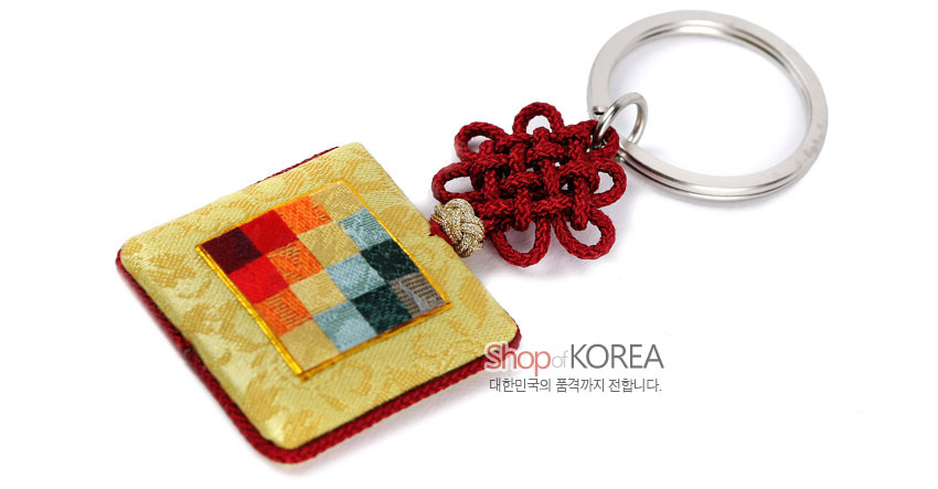 [텍스트: Shop of KOREA 대한민국의 품격까지 전합니다.] 황색 비단 바탕에 다색 조각보 패치워크가 놓인 사각 장식과 붉은 전통 매듭, 금속 링이 조화된 열쇠고리 구성