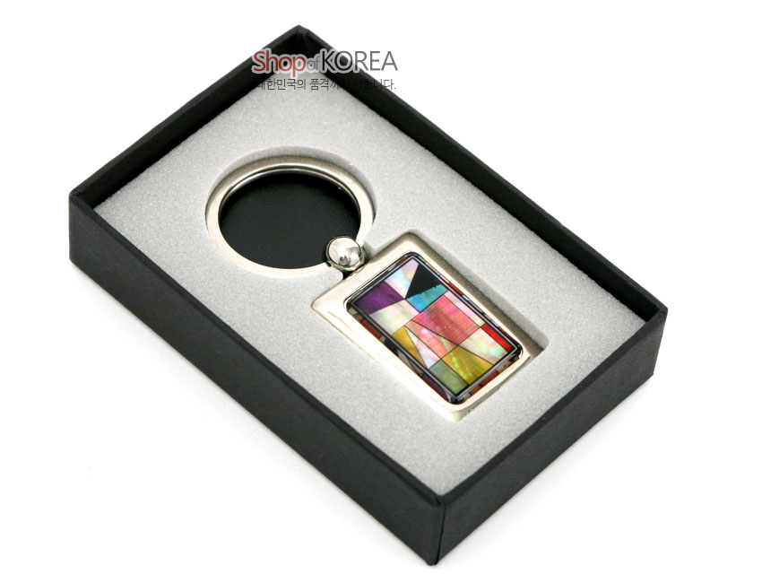 [텍스트: Shop of KOREA 대한민국의 품격, 전통을 담다.] 금속 사각 프레임에 다채로운 채색 자개를 상감하여 조각보 기하학 문양을 표현한 열쇠고리 모습