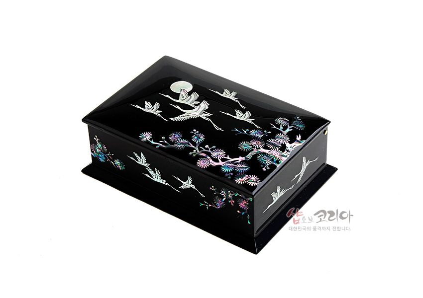 [텍스트: 샵오브코리아 대한민국의 품격까지 전합니다.] 흑색 옻칠 바탕에 자개 상감 기법으로 학과 소나무, 국화와 달 문양을 장식한 직사각형 나전칠기 명함함 이미지 설명