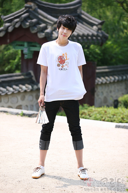 [텍스트: KOREA] 흰색 면 티셔츠 중앙 전통 탈 캐릭터 3D 발포 프린트, 갈색·주황색 계열 입체 가면 문양과 한글 캘리그래피 조합 그래픽 디자인