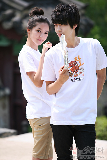 [텍스트: KOREA] 흰색 면 티셔츠 위 전통 탈 캐릭터와 타원형 문양의 3D 발포 프린트, 갈색·주황색 계열 색채 대비가 돋보이는 반소매 티셔츠 연출 이미지