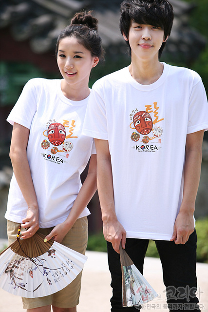 [텍스트: Korea 탈 MASK] 흰색 면 티셔츠 위 전통 탈 캐릭터와 한글·영문 조합의 3D 발포 프린트, 주황·갈색·베이지 색조의 가면 문양 장식 이미지 설명