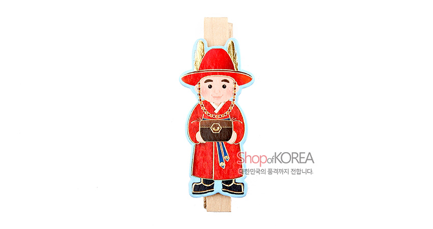 [텍스트: Shop of KOREA 대한민국의 품격까지 전합니다.] 나무 집게 위 붉은색 전통 장군 복식 캐릭터 장식, 금색 장식과 청색 테두리 대비가 돋보이는 메모 자석집게 모습
