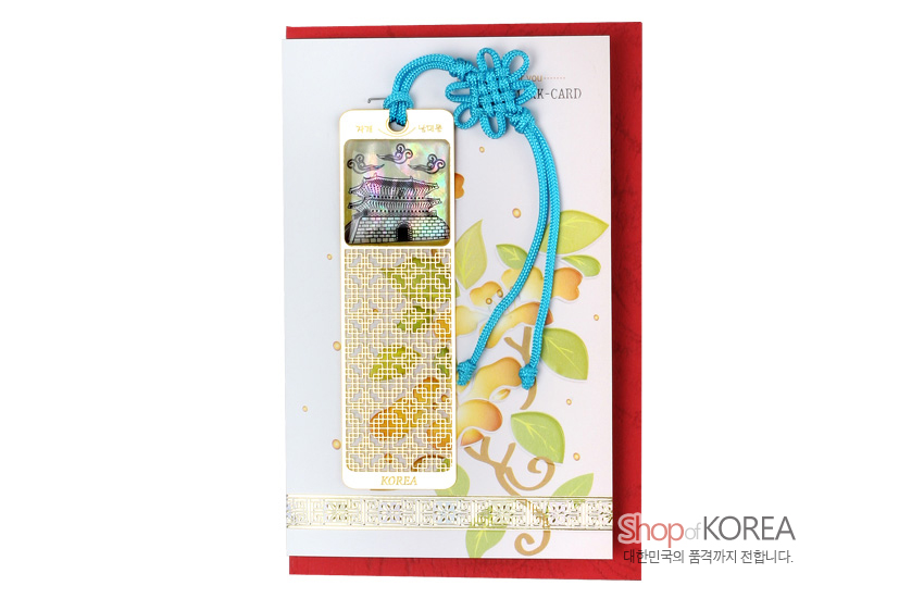 [텍스트: 자개 북카드, 수기_남대문, KOREA, Shop of KOREA, 대한민국의 품격까지 전합니다.] 자개 상감으로 표현한 남대문과 구름 문양, 금속 문살 격자무늬, 청색 전통 매듭 끈 장식의 금장 책갈피 이미지