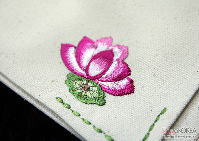 [텍스트: Shop of KOREA 대한민국의 품격까지 전달합니다] 아이보리 광목 위 연분홍·진분홍 연꽃과 초록 연잎 자수, 가장자리 초록 색실 스티치가 포인트인 전통 문양 식탁보 디테일 묘사
