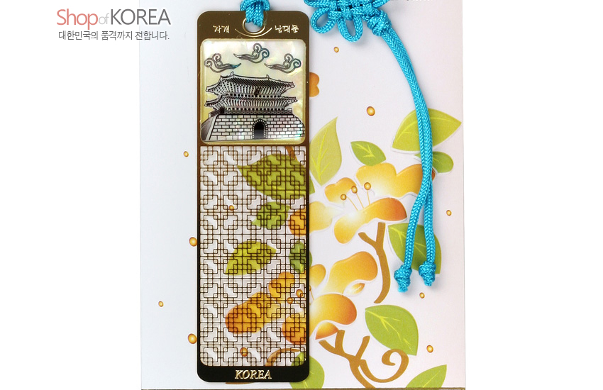 [텍스트: Shop of KOREA, 대한민국의 품격까지 전합니다., 자개, 남대문, KOREA] 금속 바탕 위 자개 상감 남대문 전경과 구름 문양, 문살 격자와 단풍잎 문양, 청색 전통 매듭끈 장식 책갈피 이미지 설명