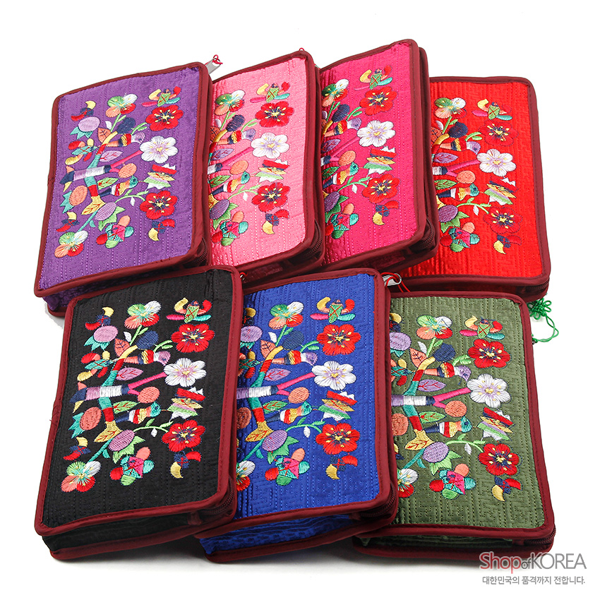[텍스트: Shop of KOREA 대한민국의 품격까지 전합니다.] 비단 누빔 바탕 위 다채로운 색실로 수복 문자와 꽃, 나비, 잎사귀 문양을 수놓은 직사각형 파우치들 모습