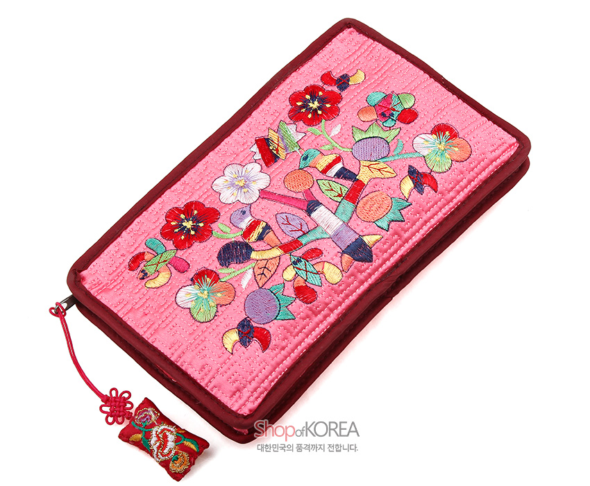 [텍스트: Shop of KOREA 대한민국의 품격까지 전합니다.] 연분홍 비단 누비 바탕에 다채로운 색실로 수복 문자와 꽃, 열매, 잎사귀 문양을 수놓은 직사각형 파우치와 노리개형 매듭 장식 구성