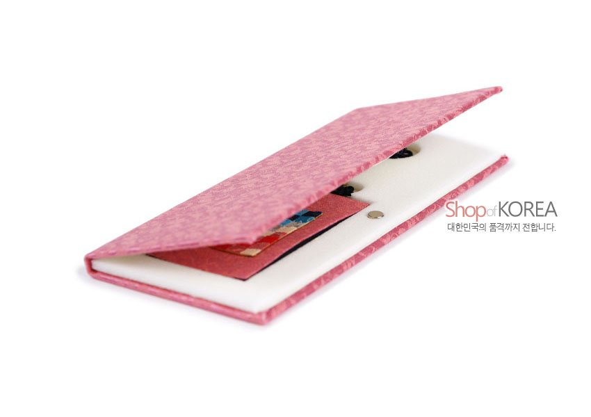 [텍스트: Shop of KOREA 대한민국의 품격까지 전합니다.] 분홍색 전통 문양 비단 케이스 안에 다채로운 색상의 조각보 장식과 검은 전통 매듭이 달린 책갈피가 놓인 모습