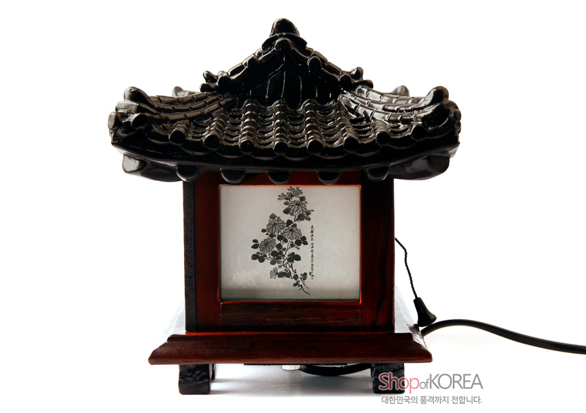 [텍스트: Shop of KOREA 대한민국의 품격까지 전합니다.] 짙은 갈색 목재 받침과 검은색 기와 지붕을 형상화한 한옥 형태 좌등, 반투명 창호지에 수묵 담채 꽃과 잎 문양을 새긴 조명 인테리어 소품