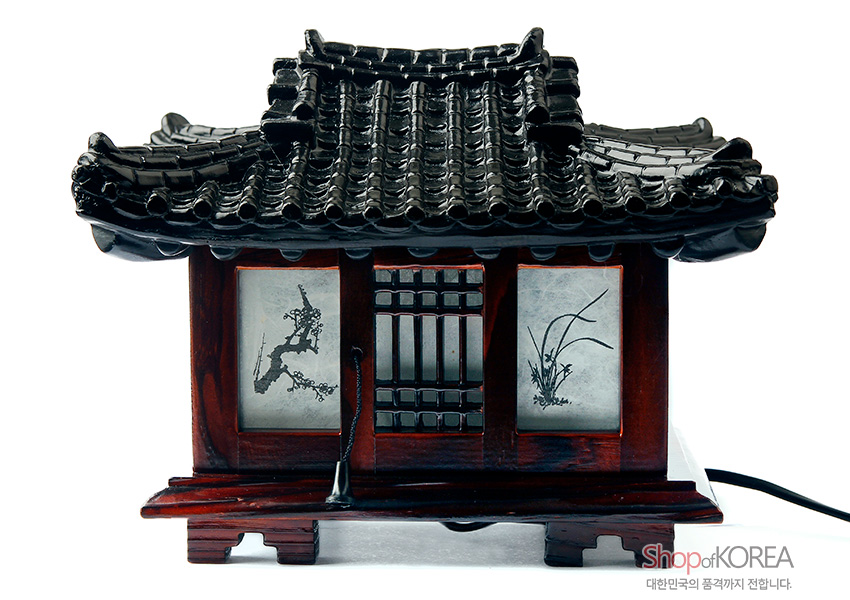[텍스트: Shop of KOREA, 대한민국의 품격까지 전합니다.] 짙은 갈색 목재와 검은 기와 지붕으로 구성된 한옥 형태 좌등, 반투명 창호에 수묵 매화와 난초 문양 장식